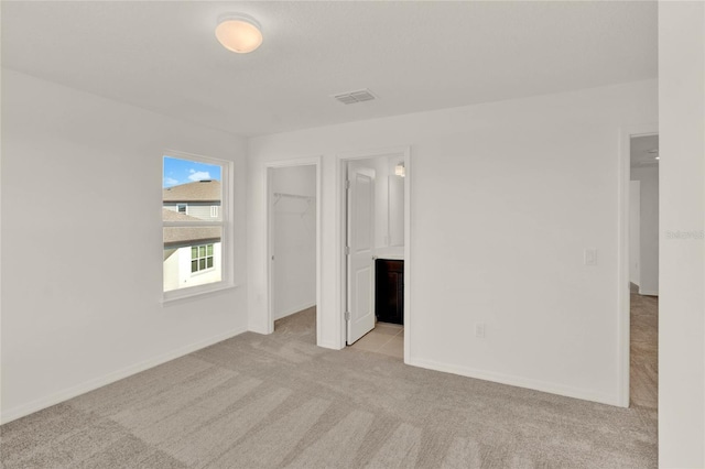 unfurnished bedroom with light colored carpet, a walk in closet, connected bathroom, and a closet