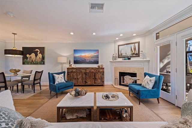 living room with a tile fireplace, ornamental molding, and light hardwood / wood-style floors