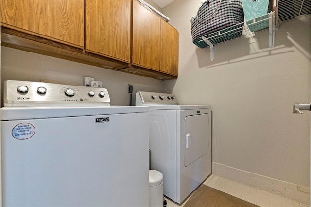 clothes washing area with light tile patterned flooring, baseboards, washer and dryer, and cabinet space