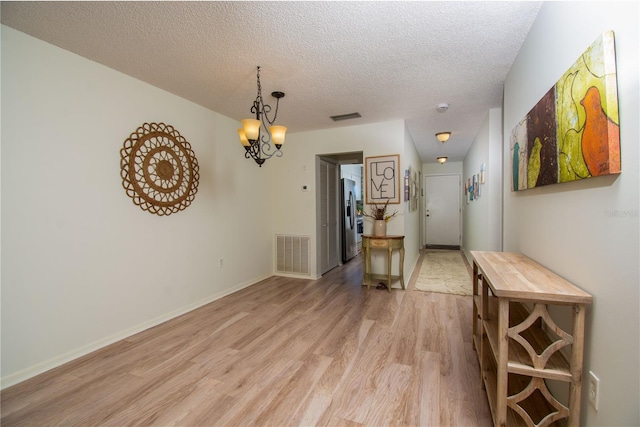 interior space with a chandelier, a textured ceiling, and light hardwood / wood-style floors