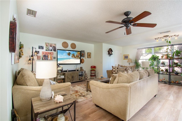 living room with ceiling fan, a textured ceiling, and light wood-type flooring