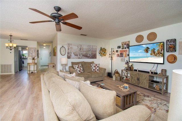 living room with ceiling fan with notable chandelier, light hardwood / wood-style floors, and a textured ceiling