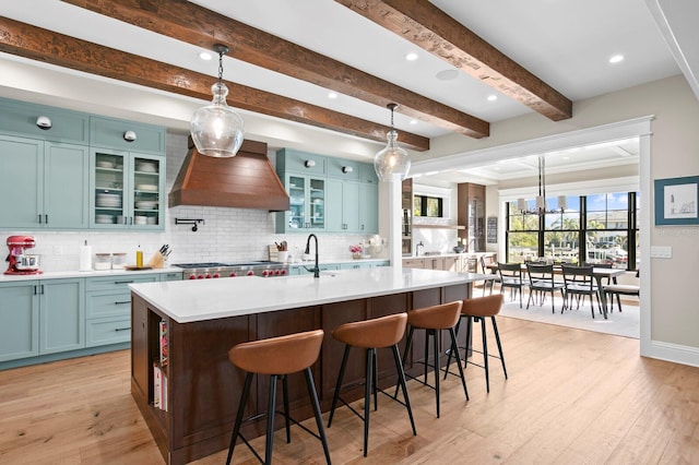 kitchen featuring pendant lighting, a center island with sink, a breakfast bar, and custom range hood