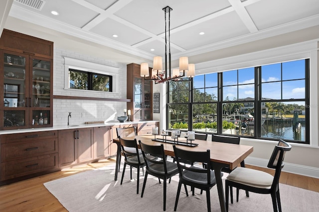 dining room with light hardwood / wood-style flooring, a water view, and coffered ceiling