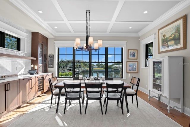 dining space featuring coffered ceiling, light wood-type flooring, a chandelier, crown molding, and a water view