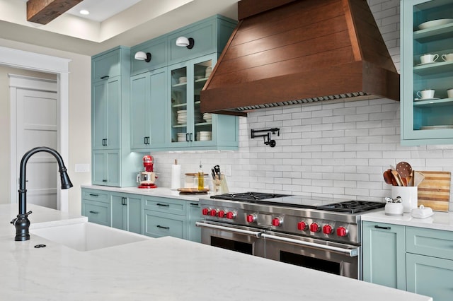 kitchen with beam ceiling, decorative backsplash, sink, range with two ovens, and custom range hood