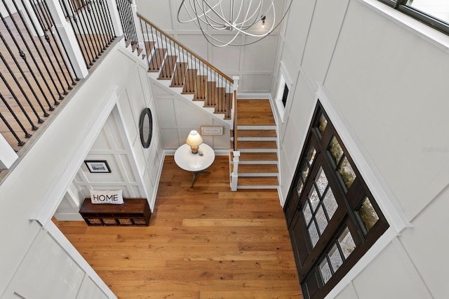 staircase with hardwood / wood-style floors, a towering ceiling, and an inviting chandelier