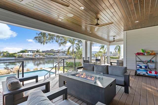 wooden terrace with ceiling fan, a water view, and an outdoor living space with a fire pit