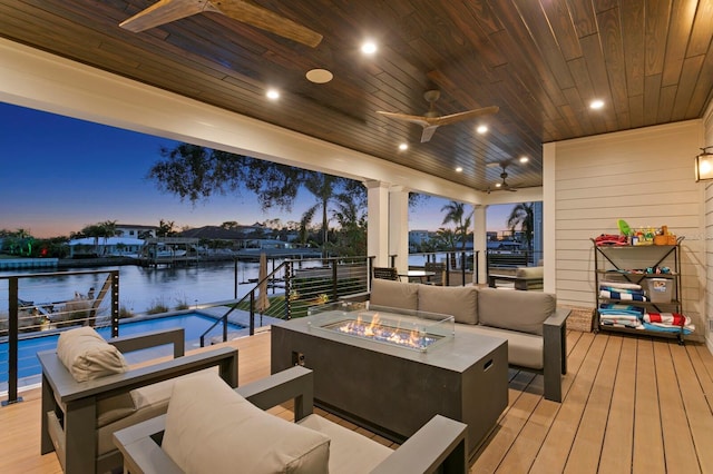 deck at dusk featuring ceiling fan, a water view, and an outdoor living space with a fire pit