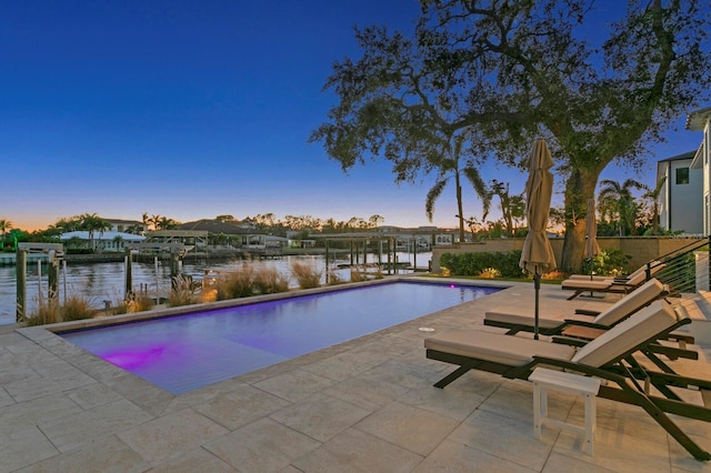 pool at dusk with a boat dock, a water view, and a patio