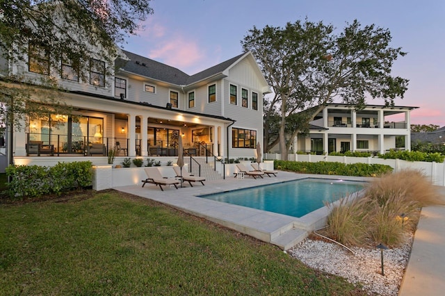 back house at dusk featuring a fenced in pool, a patio area, and a lawn