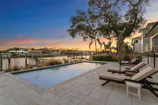 pool at dusk with a patio area and a water view