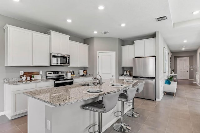 kitchen featuring a breakfast bar, stainless steel appliances, a kitchen island with sink, sink, and white cabinets