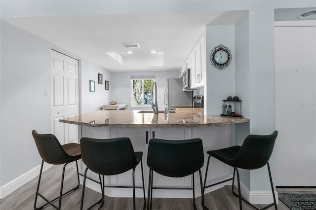 kitchen featuring white cabinets, a breakfast bar area, light hardwood / wood-style floors, kitchen peninsula, and stainless steel appliances