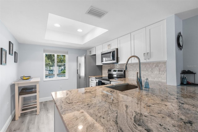 kitchen with kitchen peninsula, sink, appliances with stainless steel finishes, light stone counters, and white cabinetry