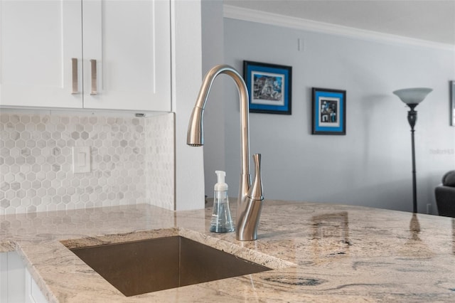 interior details with backsplash, light stone counters, crown molding, sink, and white cabinetry