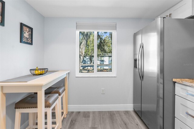 kitchen with light hardwood / wood-style floors, white cabinetry, light stone counters, and stainless steel fridge with ice dispenser