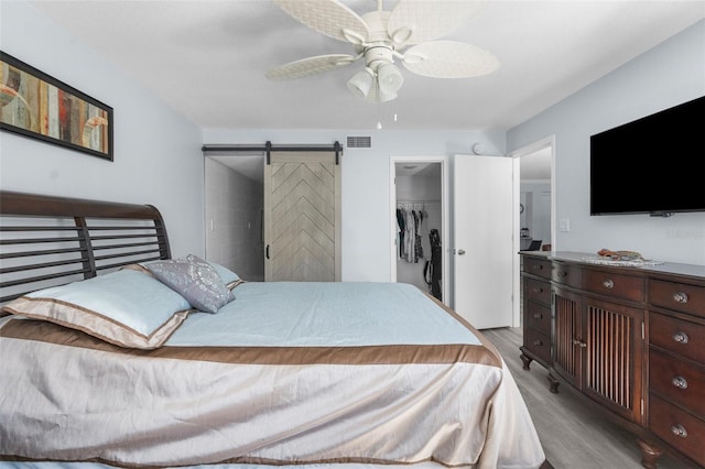 bedroom with ceiling fan, a barn door, a spacious closet, light wood-type flooring, and a closet