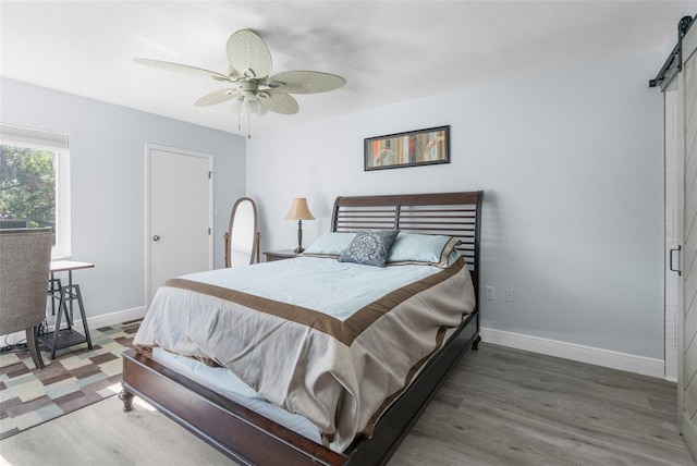 bedroom featuring a barn door, ceiling fan, and dark wood-type flooring