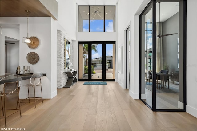 foyer entrance with light wood-type flooring, a high ceiling, and french doors