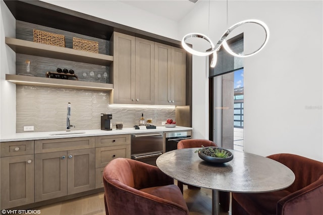 kitchen with tasteful backsplash, stainless steel dishwasher, sink, decorative light fixtures, and light hardwood / wood-style flooring