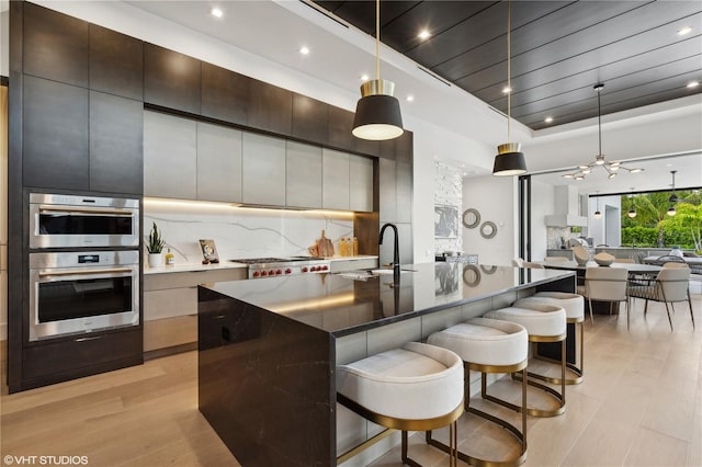 kitchen featuring sink, hanging light fixtures, an island with sink, light wood-type flooring, and appliances with stainless steel finishes