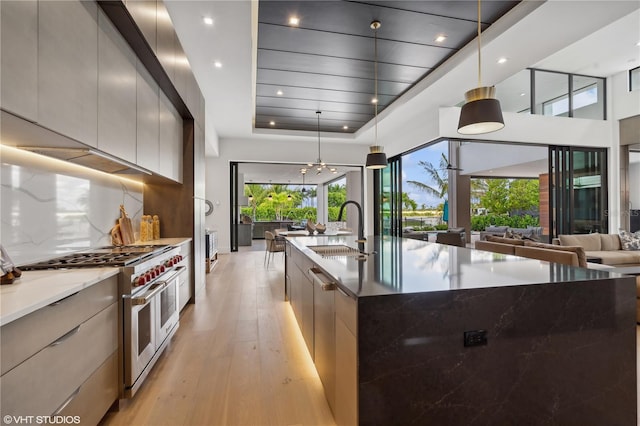 kitchen with double oven range, dark stone counters, sink, hanging light fixtures, and a large island