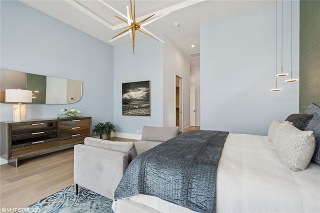 bedroom with a towering ceiling, light wood-type flooring, and an inviting chandelier