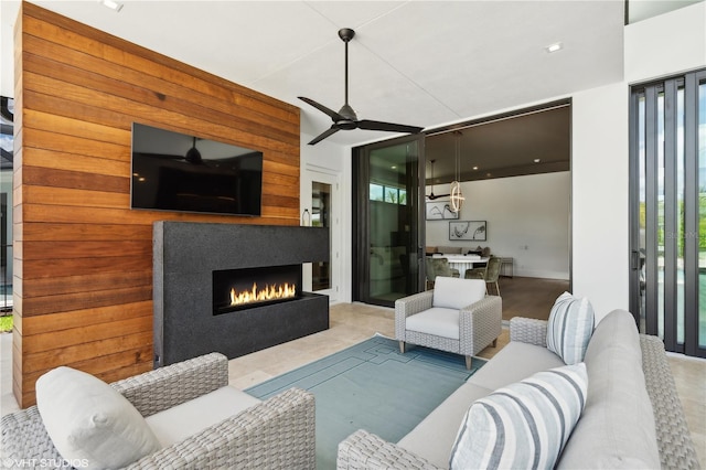 living room with ceiling fan, wooden walls, and exterior fireplace