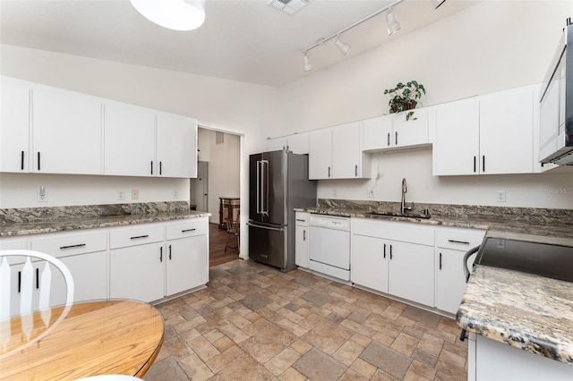 kitchen with appliances with stainless steel finishes, sink, dark stone countertops, white cabinets, and lofted ceiling