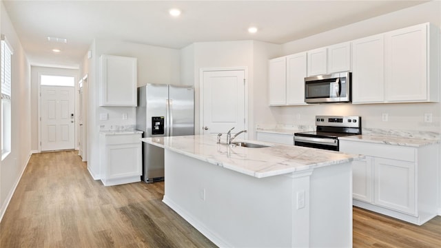 kitchen featuring light wood-type flooring, stainless steel appliances, sink, white cabinets, and an island with sink