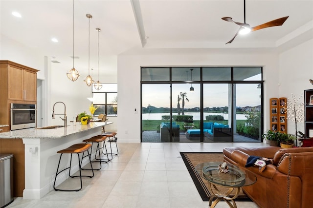 living room with a water view, ceiling fan, a tray ceiling, and sink