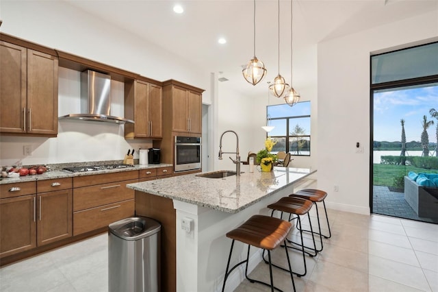 9132 Bernini Pl, Sarasota, FL 34240 - kitchen with wall chimney range hood, stainless steel appliances, a sink, brown cabinetry, and light stone counters