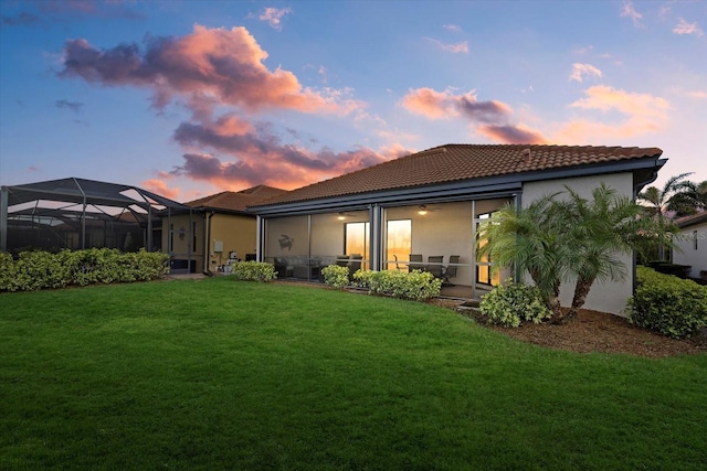 back house at dusk with glass enclosure and a yard