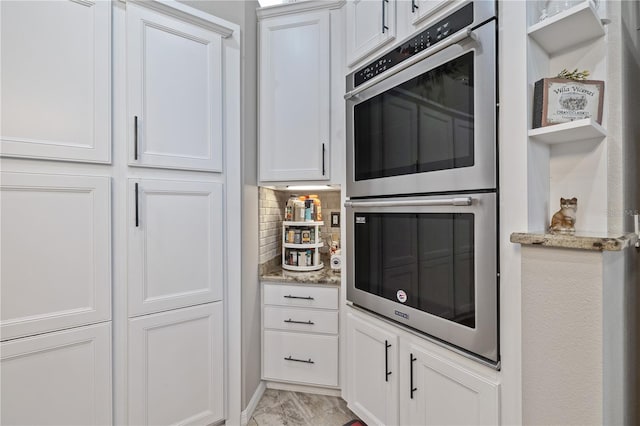 kitchen with light stone countertops, decorative backsplash, stainless steel double oven, and white cabinetry