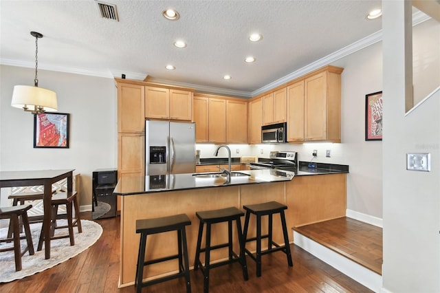 kitchen with appliances with stainless steel finishes, pendant lighting, light brown cabinetry, sink, and dark wood-type flooring