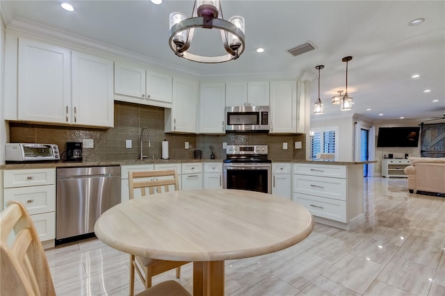 kitchen with light stone counters, white cabinets, hanging light fixtures, and appliances with stainless steel finishes