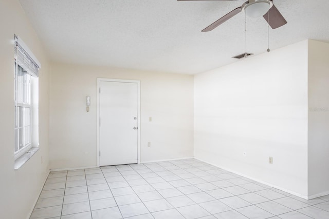 empty room featuring ceiling fan, light tile patterned floors, and a textured ceiling