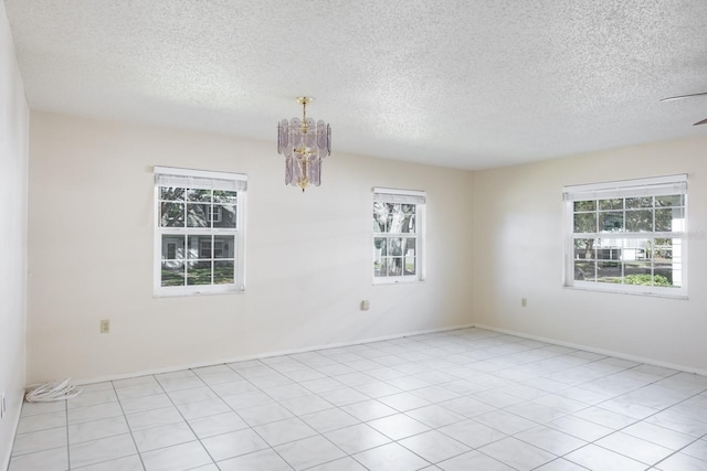 empty room with light tile patterned floors, a chandelier, and a textured ceiling