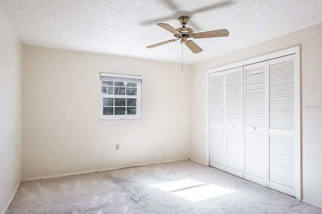 unfurnished bedroom with ceiling fan, a closet, light colored carpet, and a textured ceiling