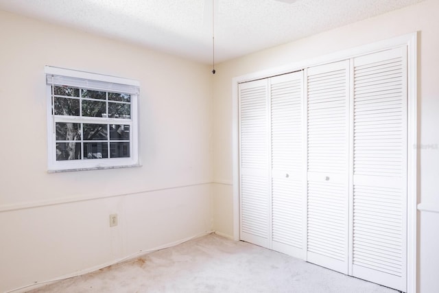 unfurnished bedroom with a textured ceiling, light carpet, and a closet