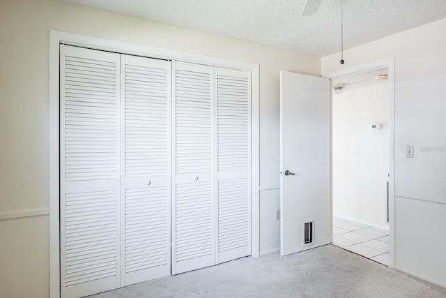 unfurnished bedroom featuring ceiling fan, a closet, light colored carpet, and a textured ceiling