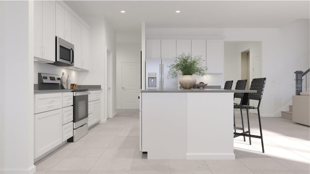 kitchen with stainless steel appliances, light tile patterned floors, a kitchen island, a kitchen bar, and white cabinets