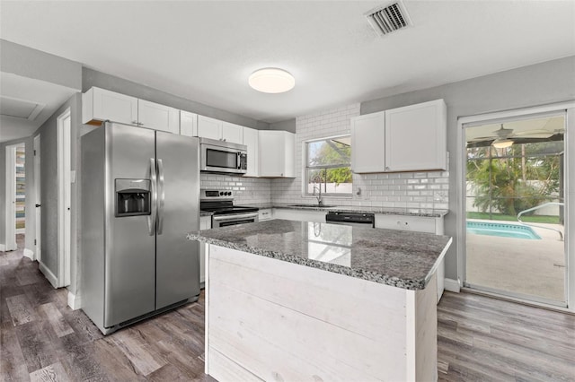 kitchen featuring appliances with stainless steel finishes, dark stone counters, sink, white cabinets, and a kitchen island