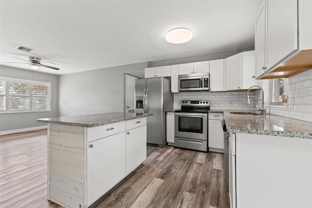 kitchen with appliances with stainless steel finishes, dark wood-type flooring, sink, white cabinets, and a kitchen island