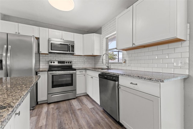 kitchen featuring white cabinets, light wood-type flooring, stainless steel appliances, and backsplash