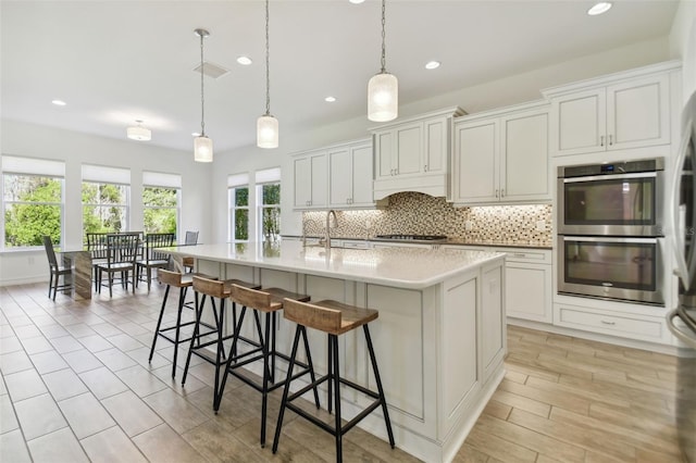 kitchen featuring decorative light fixtures, an island with sink, white cabinetry, and stainless steel appliances