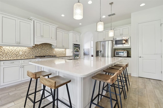 kitchen featuring appliances with stainless steel finishes, a kitchen bar, white cabinetry, and an island with sink