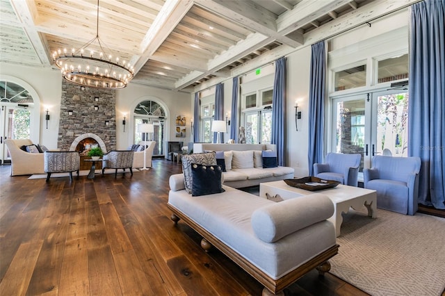 living room featuring a stone fireplace, dark wood-type flooring, french doors, a chandelier, and beamed ceiling