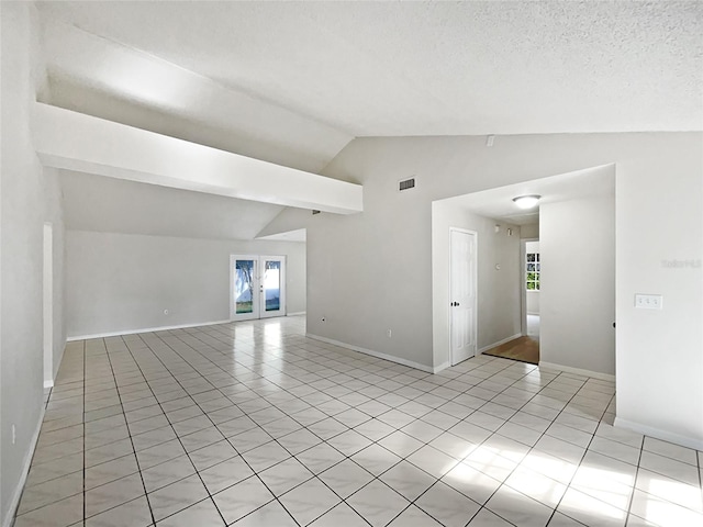 tiled spare room featuring french doors, a textured ceiling, and lofted ceiling